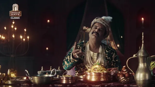 A royal-looking man in traditional attire sits at a lavish dining table enjoying biryani, highlighting India Gate’s humorous take on the “royal biryani” narrative.