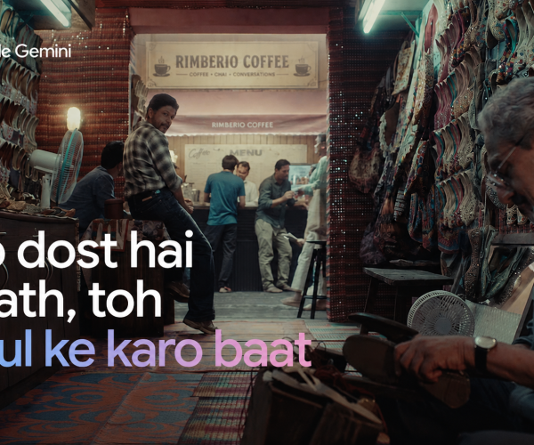 A warm, cinematic scene inside a traditional footwear shop with colorful juttis displayed along the walls, people gathered around a coffee counter, and an artisan working in the foreground. The image features the message, “Ab dost hai saath, toh khul ke karo baat.”