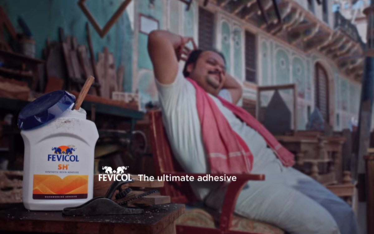 A classic Fevicol advertisement scene featuring a carpenter relaxing on a sturdy wooden chair beside a Fevicol adhesive container, showcasing why Piyush Pandey’s Fevicol storytelling still feels like a marketing miracle.