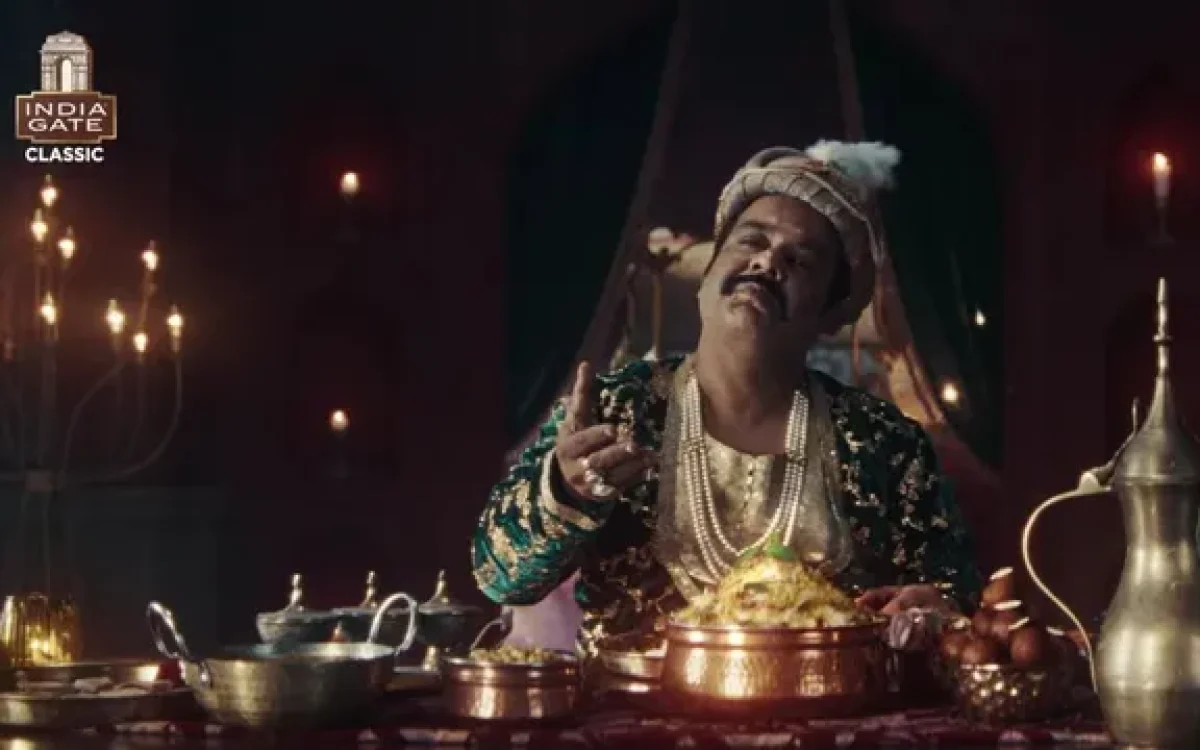 A royal-looking man in traditional attire sits at a lavish dining table enjoying biryani, highlighting India Gate’s humorous take on the “royal biryani” narrative.
